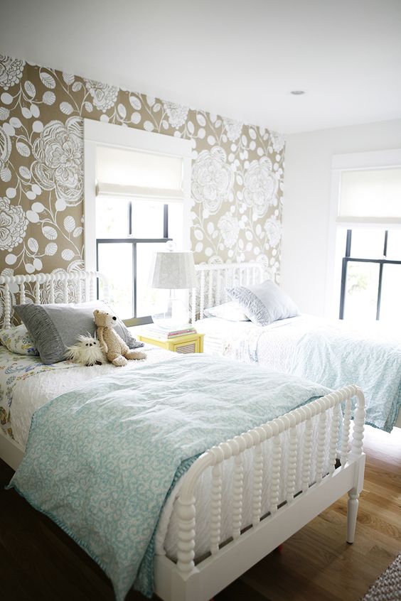a lovely pastel shared girl bedroom with an accent botanical wall, white wooden beds, blue and grey bedding, a bright nightstand and a table lamp a lovely pastel shared girl bedroom with an accent botanical wall, white wooden beds, blue and grey bedding, a bright nightstand and a table lamp