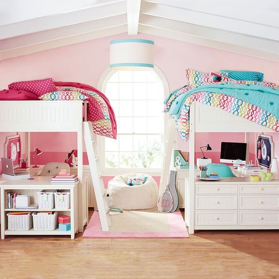 a pink shared girls' bedroom with two white bunk beds, with colorful bedding, desks and chairs under the beds and dressers for storage is a creative solution for a small room