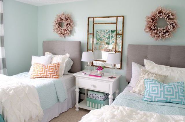 a stylish pastel girls' bedroom with light blue walls, grey upholstered beds, blue and white bedding and pillows, fabric wreaths and a framed mirror on the nightstand a stylish pastel girls' bedroom with light blue walls, grey upholstered beds, blue and white bedding and pillows, fabric wreaths and a framed mirror on the nightstand