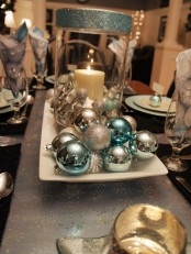 a sparkling Christmas centerpiece of a plate with blue and silver ornaments and a candle lantern with blue glitter is very chic and easy to recreate