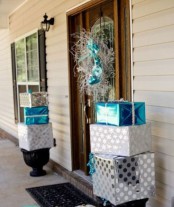 front porch Christmas decor with stacked silver and blue gift boxes and with a silver and blue wreath on the front door is amazing