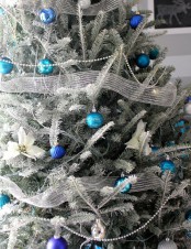 a frozen Christmas tree decorated with silver ribbons, blue, navy and black ornaments looks very spectacular and bold