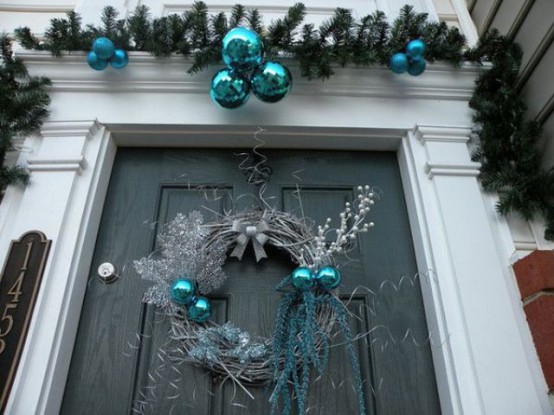 a silver and teal Christmas wreath with twigs, branches and ornaments and blue ornaments over the door for a truly winter feel