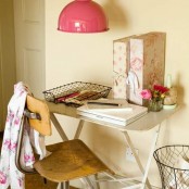 a little vintage home office nook with a neutral desk, a plywood chair, some floral files and a pink pendant lamp over it