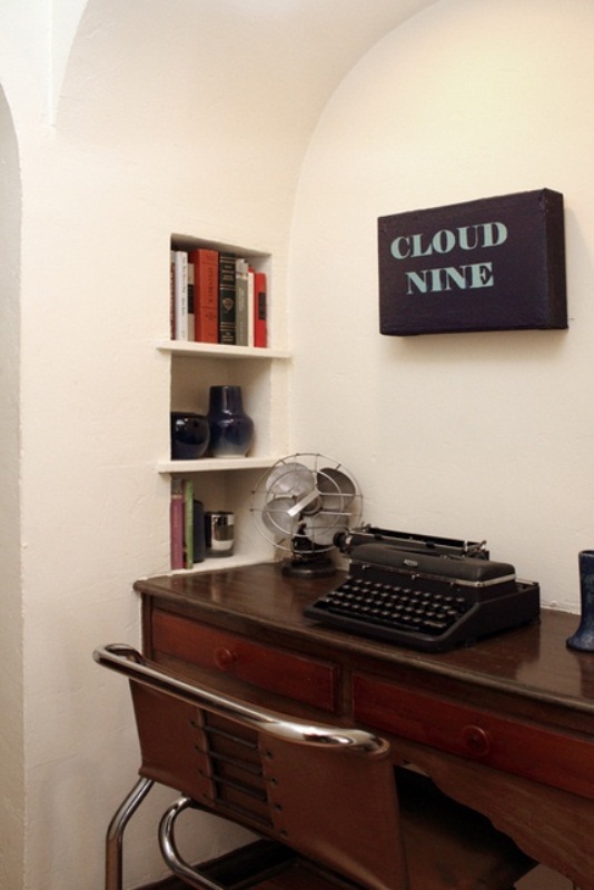 a delicate vintage home office with built-in bookshelves, a dark stained vintage desk, a leather chair, a black typewriter and a table fan