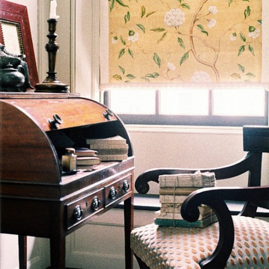 a vintage home office with a vintage stained bureau and a beautiful dark-stained chair, a bold floral curtain, candles and a mirror