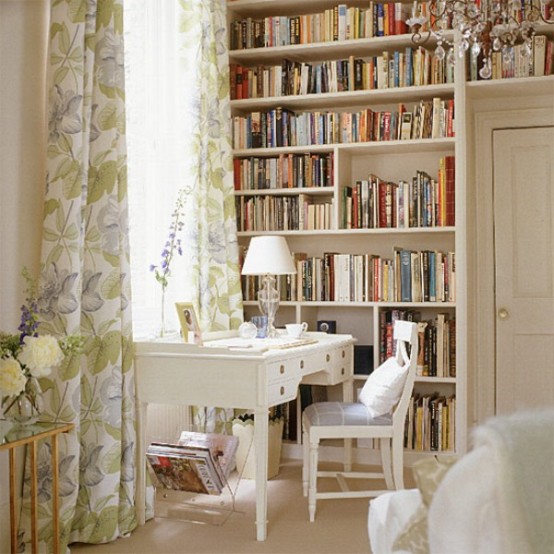 a neutral vintage home office with bookshelves, a vintage white desk and a chair, a table lamp and floral curtains and fresh pastel blooms