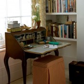 a vintage home office with built-in bookshelves, a stained vintage desk and a rust-colored stool, blooms and tin boxes for storage