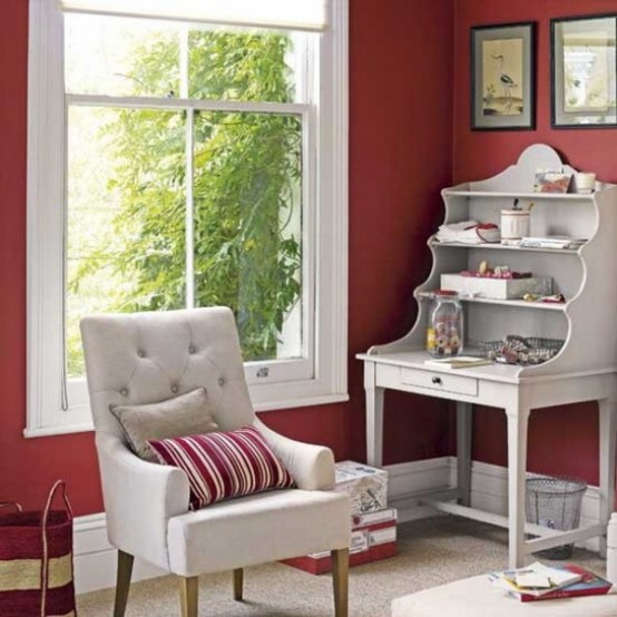 a burgundy and grey home office nook with burgundy walls, a whitewashed vintage bureau desk, a grey upholstered chair and printed pillows and a gallery wall