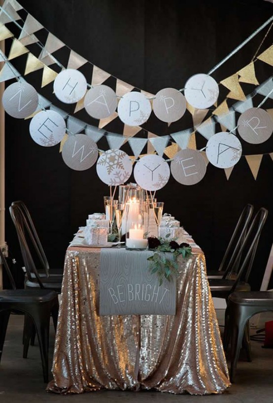 a NYE party tablescape with a gold sequin tablecloth, a neutral table runner and greenery, candles and sparkling garlands is a gorgeous space to celebrate NYE