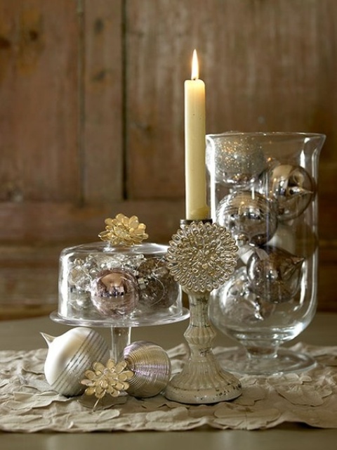 a silver NYE party centerpiece of glass bowls filled with silver ornaments, a tall and thin candle in a tall candleholder