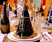 a black and gold NYE party tablescape with a gold sequin table runner, white porcelain and black and gold cone hats plus gold-rimmed glasses