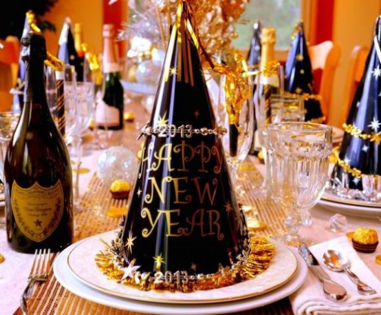 a black and gold NYE party tablescape with a gold sequin table runner, white porcelain and black and gold cone hats plus gold-rimmed glasses