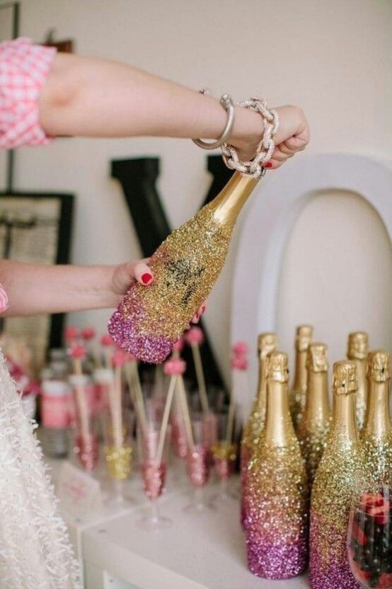champagne bottles done with gold and pink glitter with an ombre effect is a fresh and cool decor idea for a NYE party
