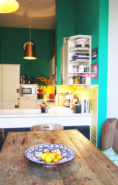 an emerald kitchen with white cabients, a yellow tile backsplash, a copper pendant lamp and a dining zone next to the space