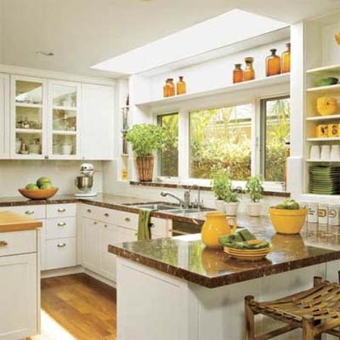 a white farmhouse kitchen with a large window, stone countertops and green textiles and plants and yellow porcelain