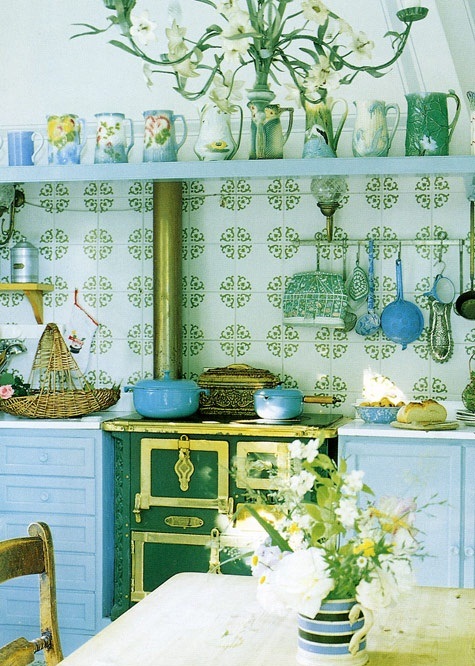 an eclectic colorful kitchen with light blue cabinets and shelves, green tiles, a green and yellow cooker and tableware and vases in the same colors