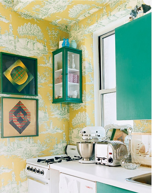 a bold kitchen with yellow printed wallpaper and sleek emerald cabinets plus white countertops and bright artworks