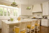 a refined white kitchen with a white marble backsplash and countertops, green pendant lamps and yellow chairs