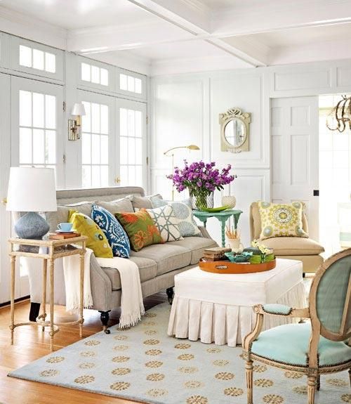 a welcoming neutral living room done with bright and colorful pillows, with a printed rug and some blooms in a vase
