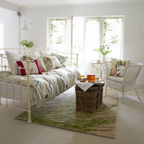 a chic vintage summer living room with floral rpint textiles, a green print rug and lots of greenery in pots and vases