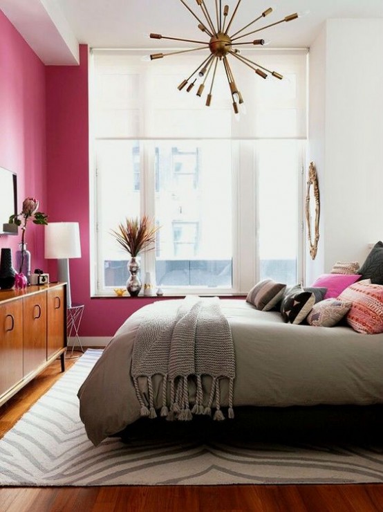 a bright and welcoming mid-century modern bedroom with a fuchsia statement wall, a rich stained dresser and a brass burst chandelier