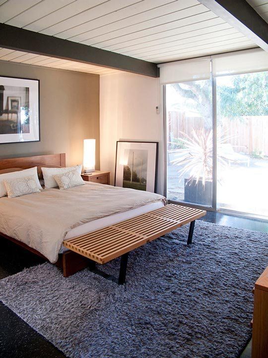 a black and white bedroom with a grey statement wall, a wooden bed, a wooden bench, a fluffy grey rug and a glazed wall