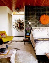 a bright mid-century modern bedroom with a cathcy black wall, a mustard chair, a fluffy rug and an orange decoration over the bed