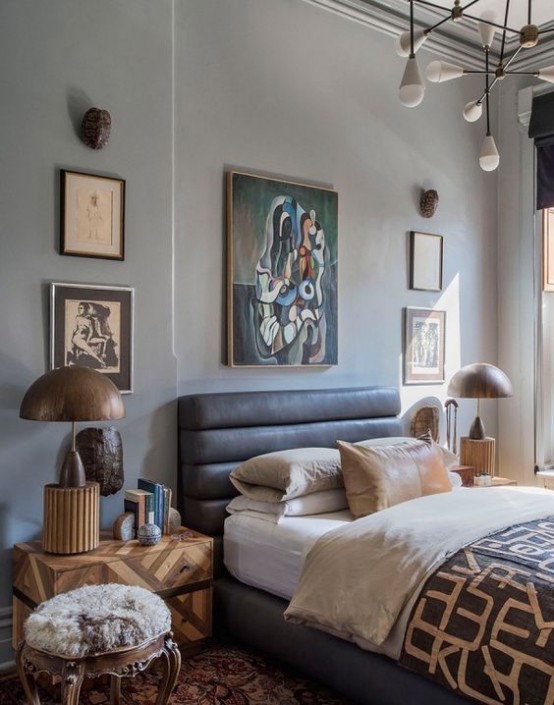 a chic and eclectic bedroom with a leather bed, matching artworks, a chic chandelier, wooden lamps and geometric nighstands plus a fur stool