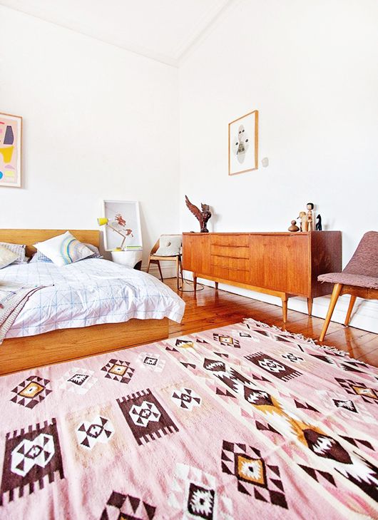 a welcoming and bright mid-century modern space with warm-stained wooden furniture, a pink rug and some artworks