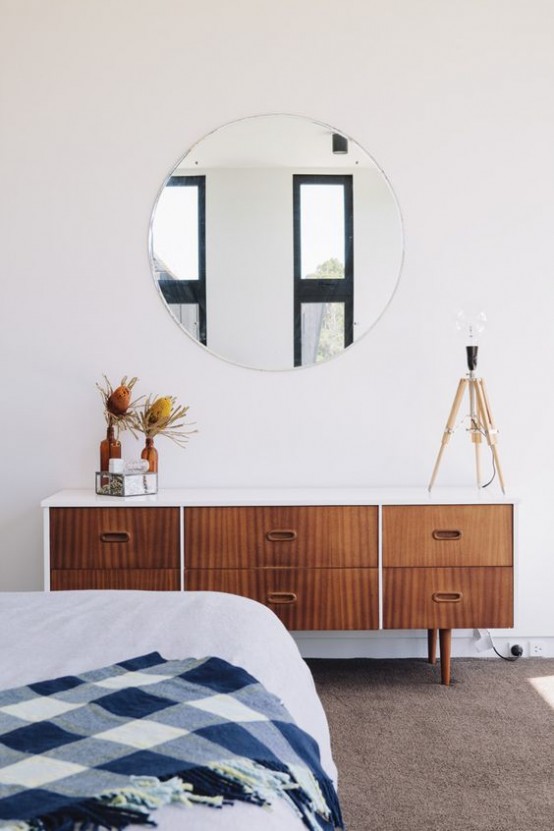 a stylish mid-century modern bedroom with a wooden dresser, a round mirror, a large bed and a rug