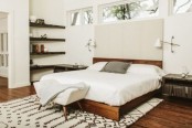 a neutral mid-century modern bedroom withs tained wooden shelves, a rich stained bed with a neutral headboard and wall lamps