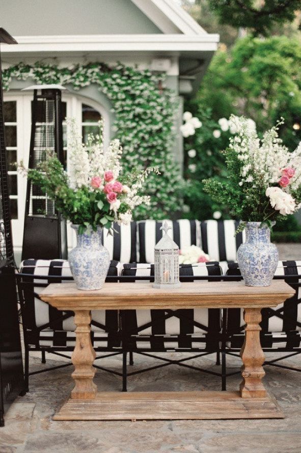 an elegant outdoor space with a striped sofa, a rustic wooden console table and lots of fresh blooms and greenery