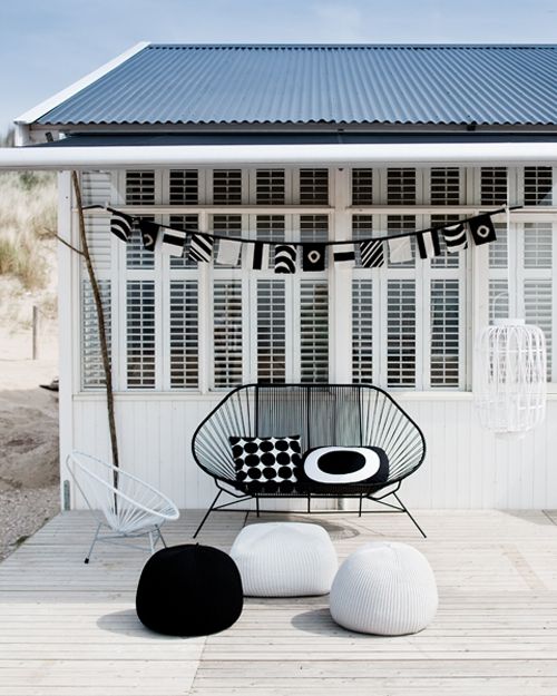 a pretty black and white outdoor space with a whitewashed desk, a black chair, black and white poufs and pillows