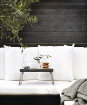 a Scandinavian terrace with black walls, a black and white sofa, a small black table for serving drinks and food