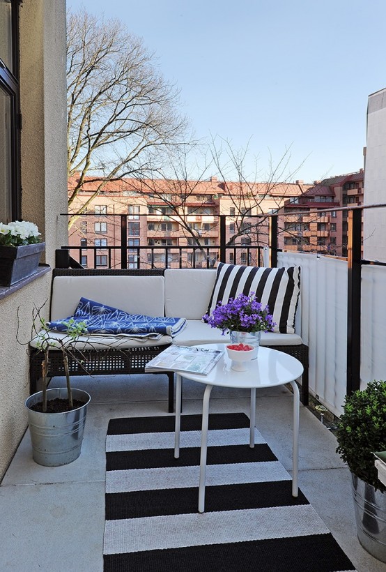 a black and white Scandinavian balcony with a wicker sofa, a white table and printed pillows and blankets