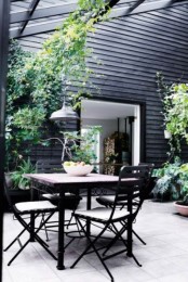 a Scandi outdoor space with black walls, a metal and wood table and black chairs and lots of greenery to visually refresh the space