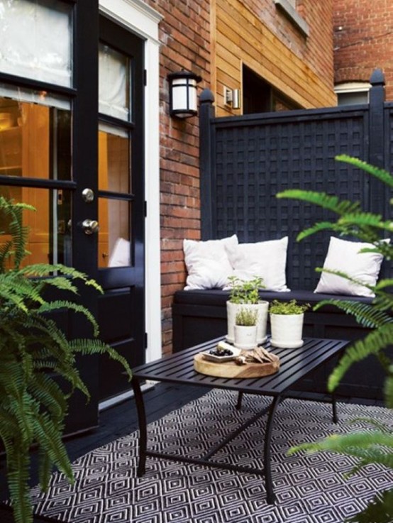 a Nordic balcony with a black wall, a black built-in bench and a wooden table, a printed chair and potted greenery to refresh the space