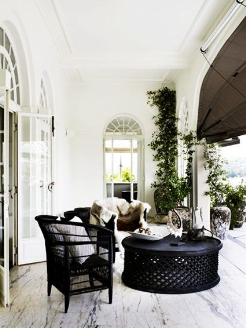 an indoor-outdoor space with black wicker and wooden furniture, with neutral upholstery, potted greenery is a very cool and chic idea