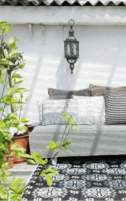 a monochromatic outdoor space with a printed sofa and printed pillows, a grey and white printed rug and some potted greenery and blooms to cheer up the space