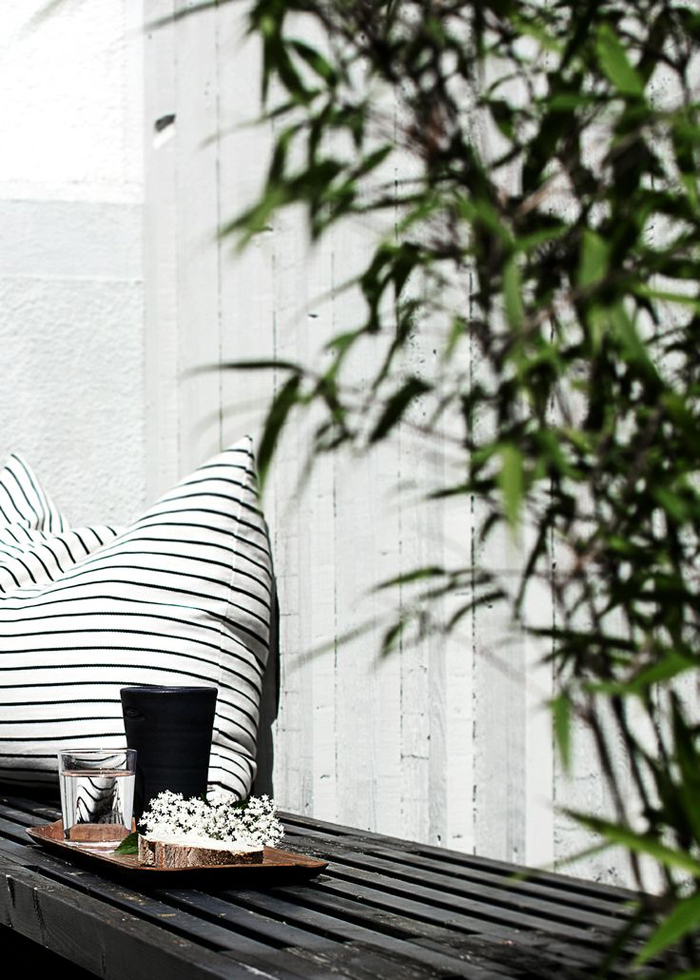 a Nordic terrace with a black bench and a striped pillow, some greenery is a beautiful idea for those who love minimalism