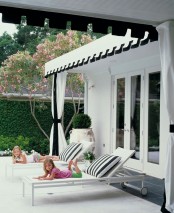 a stylish black and white pool space with black and white curtains, white loungers, striped black and white pillows