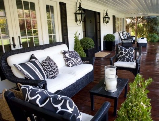 a farmhouse porch with black and white wicker furniture, printed pillows, potted greenery and pillar candles