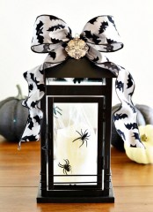 a candle lantern decorated for Halloween, with spiders inside and a bat printed ribbon bow on top