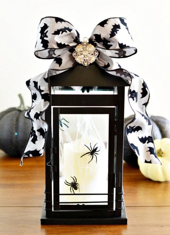 a candle lantern decorated for Halloween, with spiders inside and a bat printed ribbon bow on top
