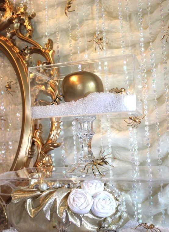 a crystal stand with a clear box and a gold apple, gold spiders and white fabric flowers for a glam Halloween party