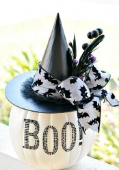 a white pumpkin with BOO letters, a black hat with a bat ribbon bow and feathers is a pretty and cute Halloween decoration