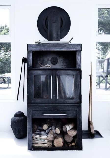 a black shabby chic fireplace with a firewood storage space makes a statement in this white space