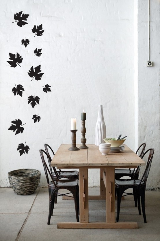a Nordic dining space with white brick walls, black leaves and a dining table with mismatching chairs
