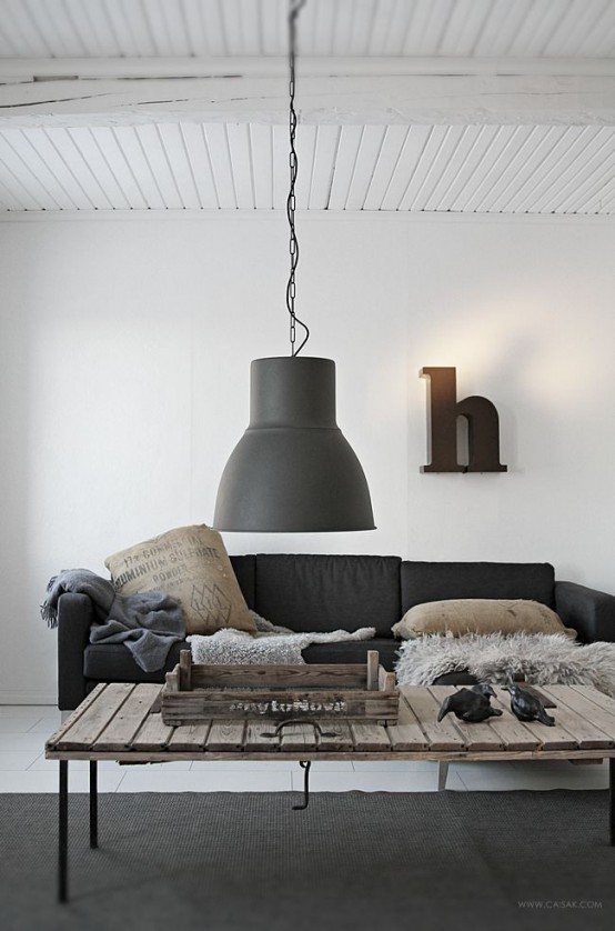 a flal Nordic living room with a black sofa, muted pillows, a pallet wood table and some faux fur